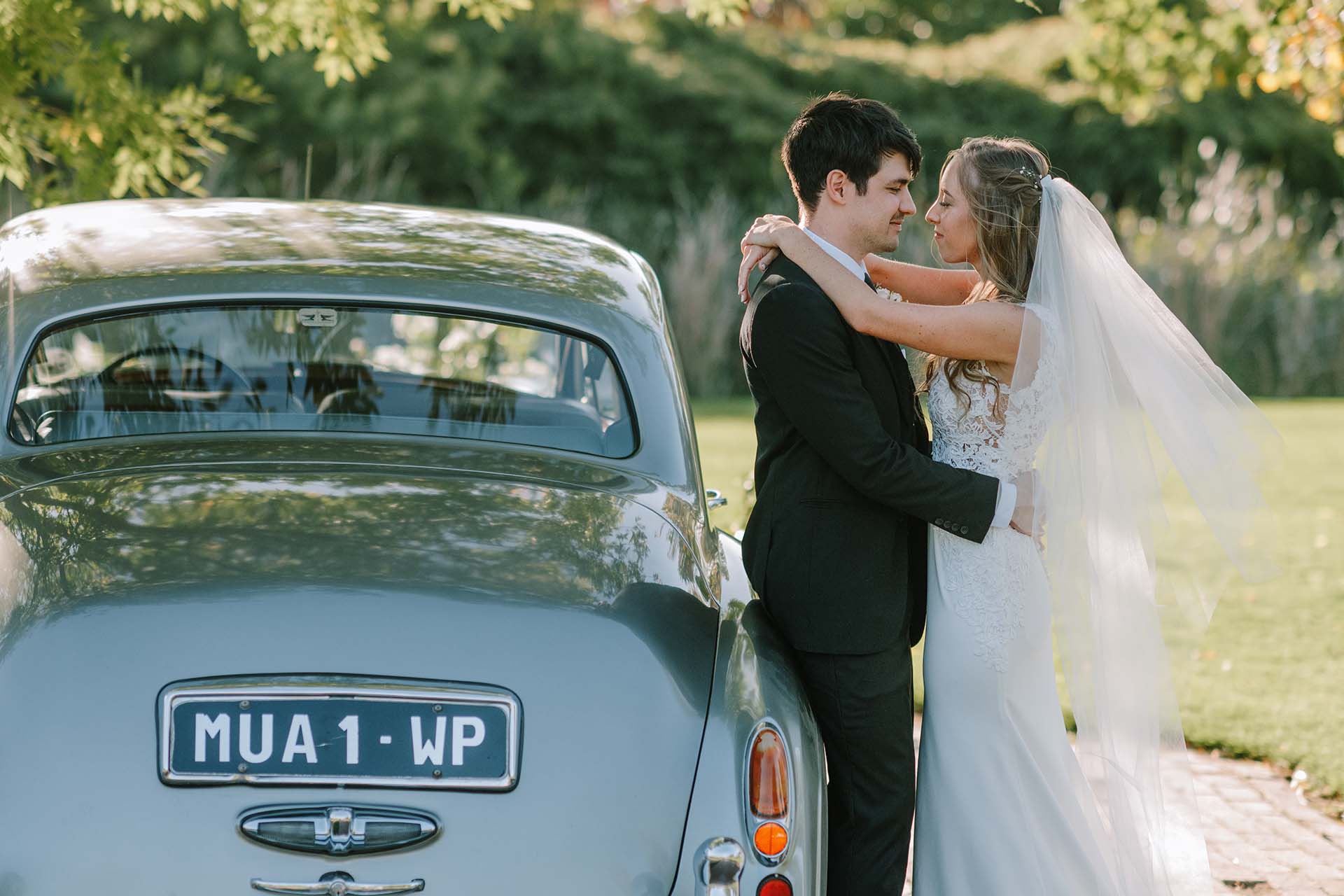 a young bride and groom standing by a teal vintage car at one of the most stunning wedding venues in the cape winelands