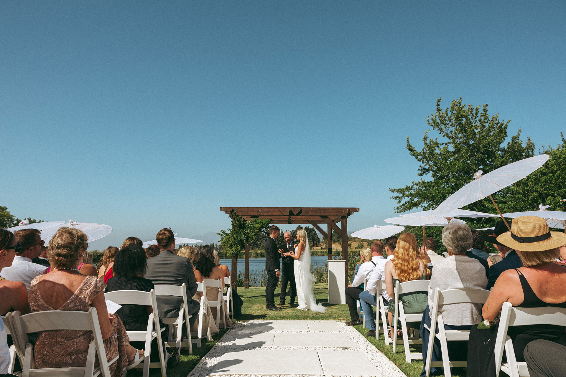 a bride and groom before an altar at their outdoor ceremony by the lake surrounded by one of the best garden wedding venues around Cape Town.