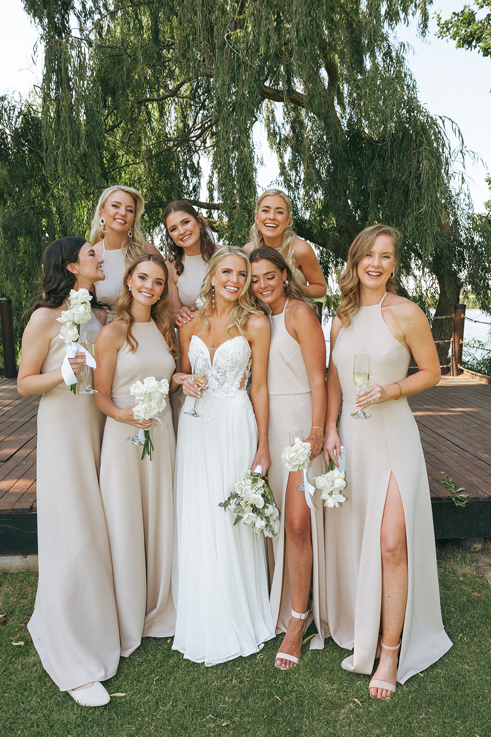 a summer bride stands amongst her bridesmaids who all wear beige dresses at Rhebokskloof which offer an elegant summer garden wedding venue.