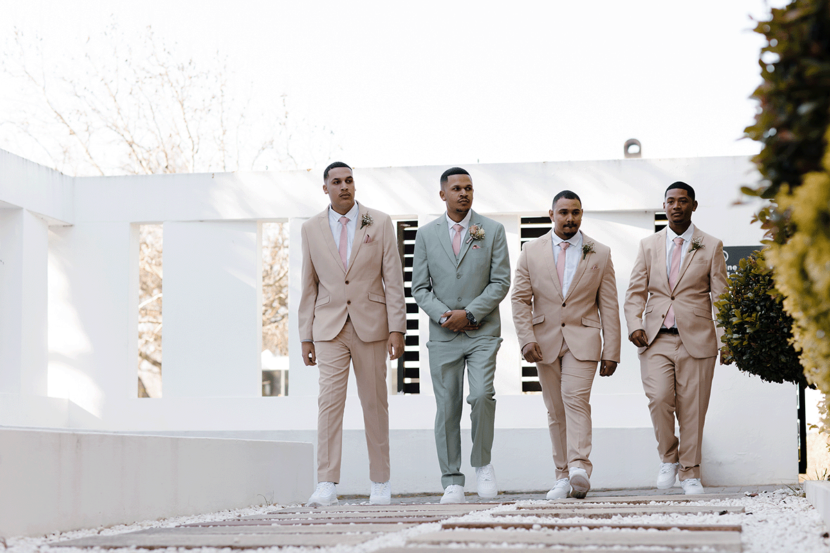 a young groom dressed in a light green suit walks with his 3 grooms men all dressed in beige.